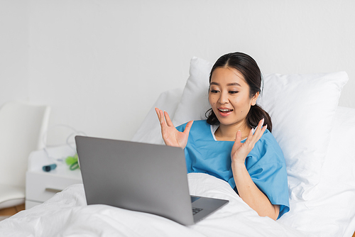amazed asian woman showing wow gesture during video call on laptop on hospital bed