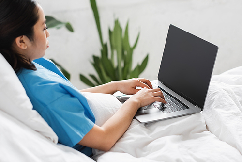 young asian woman sitting on hospital bed and typing on laptop with blank screen