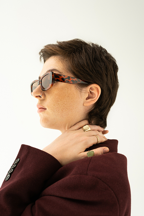 brunette woman in trendy sunglasses and finger rings looking away isolated on grey