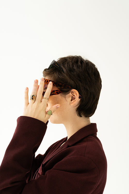 side view of brunette short haired woman in finger rings wearing several sunglasses isolated on grey