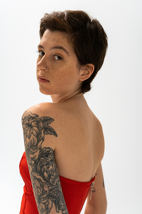 portrait of young woman with tattoo and freckles looking at camera isolated on grey