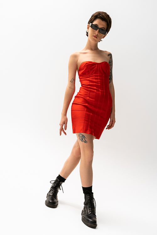 full length of tattooed woman in red strapless dress and black leather boots on grey background