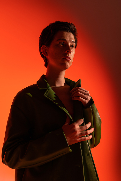 fashionable woman in green leather jacket looking away on orange shaded background