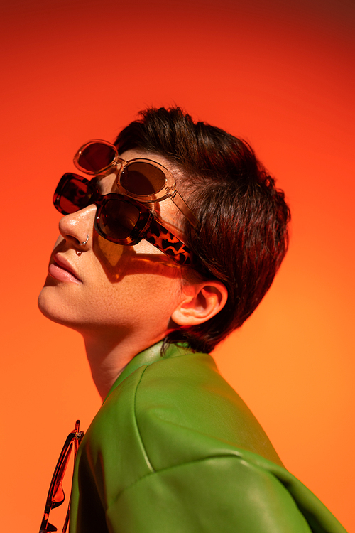 portrait of young woman with short brunette hair wearing two trendy sunglasses on orange background