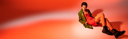 full length of stylish woman in green jacket and black rough boots posing on colorful background, banner