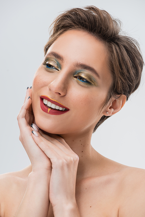 happy young woman with short hair and bright makeup looking away isolated on grey