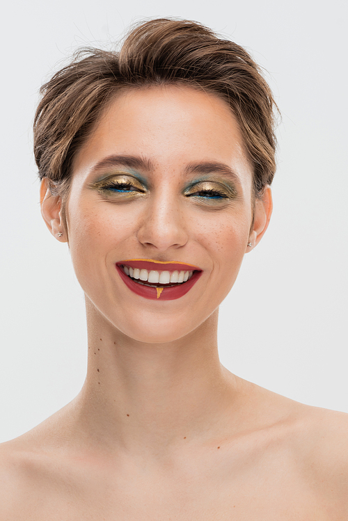 positive young woman with short hair and bright makeup looking at camera isolated on grey