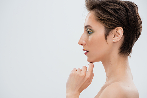 side view of young woman with bright makeup touching chin isolated on grey