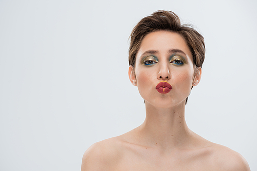 portrait of young woman with shiny makeup and short hair pouting lips isolated on grey