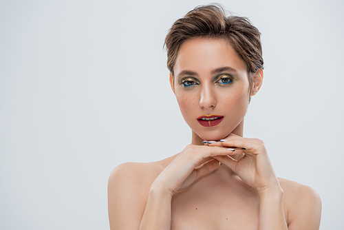 young woman with shimmery eye makeup and short hair looking at camera isolated on grey