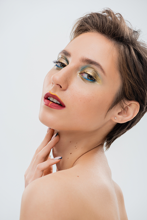 brunette young woman with shimmery eye makeup and short hair touching neck isolated on grey