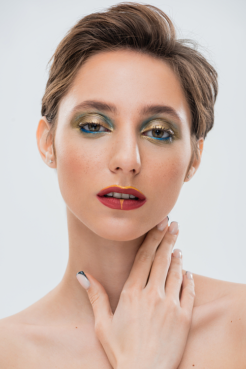 brunette young woman with shimmery eye makeup and red lips touching neck isolated on grey