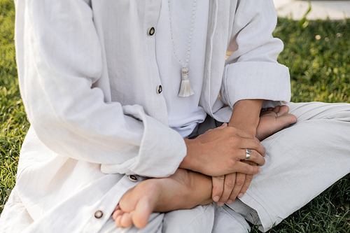 cropped view of man in white clothes sitting in lotus pose during meditation outdoors