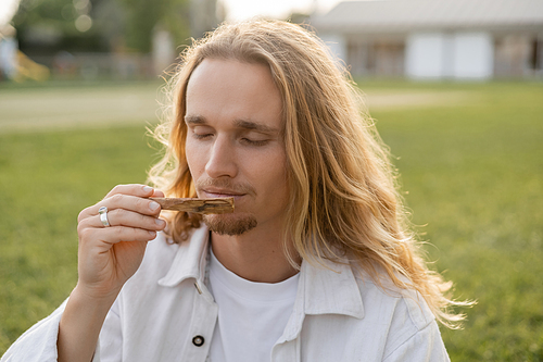 long haired yoga man with closed eyes enjoying flavor of palo santo stick outdoors