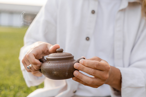 partial view of man in white cotton clothes holding oriental teapot outdoors