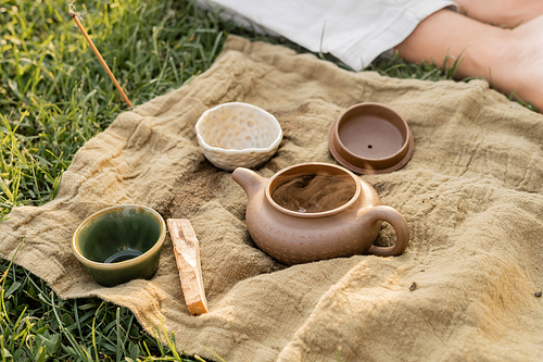 aromatic palo santo stick and ceramic teapot with cups near cropped yoga man sitting on grassy lawn