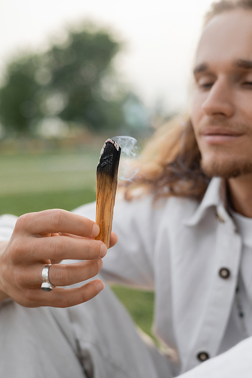 smoldering aromatic stick in hand of blurred man meditating outdoors