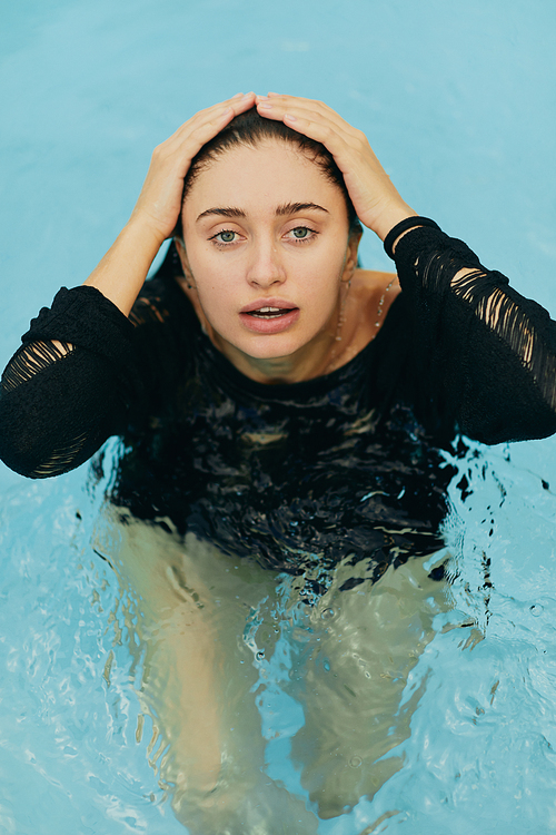 no makeup look, beautiful and sexy brunette woman in black knitted outfit posing inside of outdoor swimming pool during vacation in Miami, natural beauty, luxury resort, Florida, top view