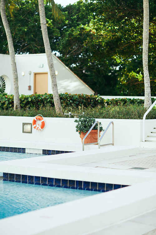 luxury resort, public swimming pool with bright blue water and metallic pool ladder with stainless handrails next to potted plant, blurred background, vacation and holiday concept, outdoor leisure