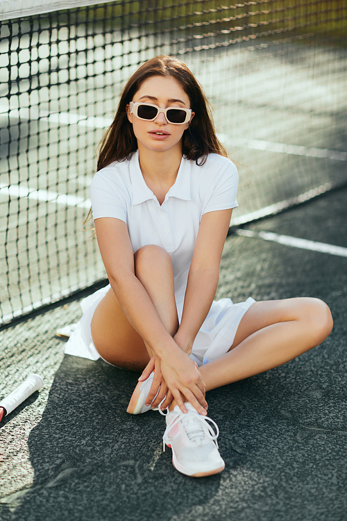 tennis court in Miami, athletic young woman with brunette long hair sitting in white outfit, shoes and sunglasses near tennis net, blurred background, iconic city, physical activity