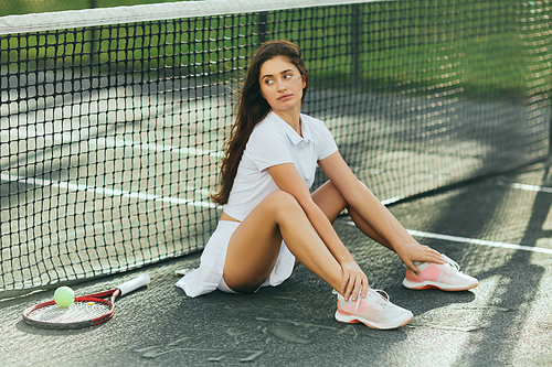 female tennis player warming up before game, young woman with long hair sitting in white outfit near racket with ball and tennis net, blurred background, Miami, iconic city, tennis court