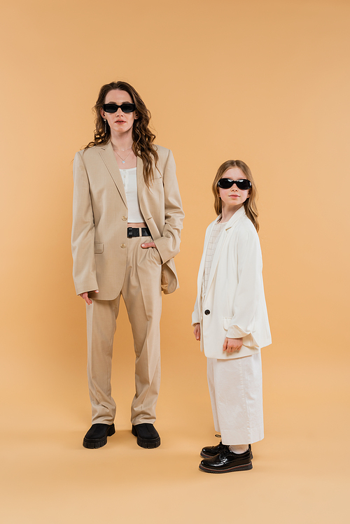 modern family, mother and daughter in sunglasses, stylish businesswoman and girl in suits posing together on beige background, fashionable outfits, formal attire, corporate mom
