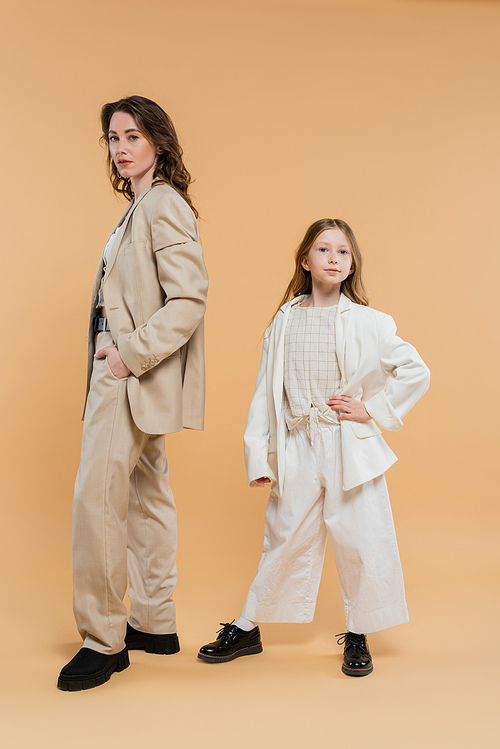 stylish mother child concept, woman in suit and preteen daughter standing in suits on beige background, corporate mom, businesswoman, posing together, hand on hip, business style