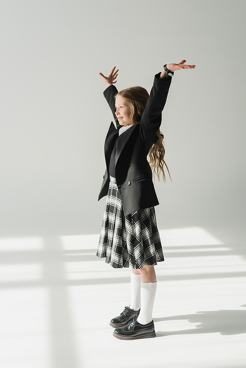 schoolgirl in uniform, cheerful preteen girl standing with raised hands on grey background, formal attire, fashionable kid, joyful, excitement, celebration of learning, back to school concept