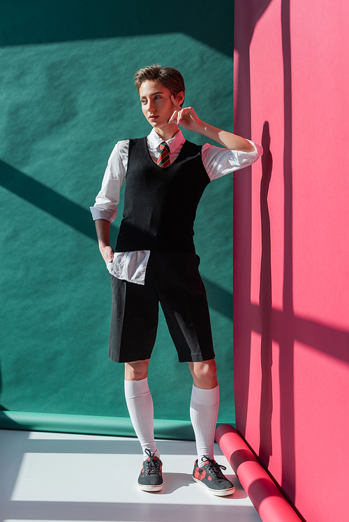 full length of young woman with short hair posing in school uniform on pink and green