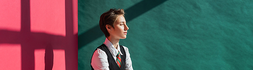 stylish young woman with short hair posing in school uniform on green and pink background with shadows, banner