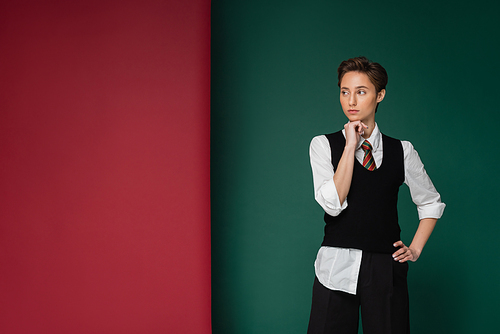 stylish young student with short hair posing with hand on hip on green and maroon background