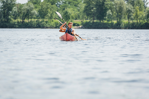 couple of sportive multiethnic friends in life vests sailing in kayak with paddles while spending summer weekend on river on blurred foreground, water recreation