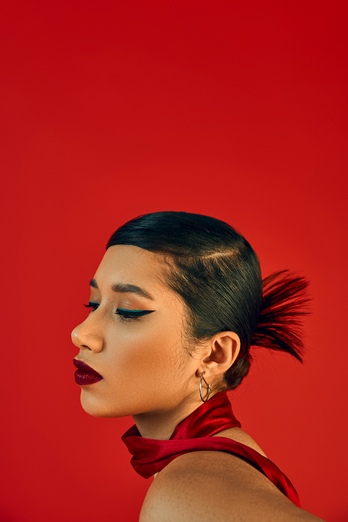 youth fashion, stylish spring concept, portrait of young and charming asian woman with brunette hair, bold makeup and trendy hairstyle posing in neckerchief on red background