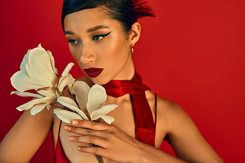 portrait of young and attractive asian woman with white blooming orchid on red background, bold makeup, brunette hair, neckerchief, spring fashion photography, elegant and charming