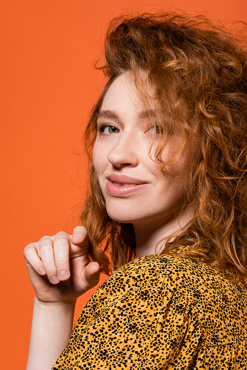Portrait of young red haired model in yellow blouse with abstract print looking at camera and standing isolated on orange, stylish casual outfit and summer vibes concept, Youth Culture
