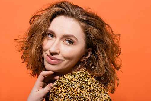 Portrait of smiling and red haired woman with natural makeup posing in yellow blouse and looking at camera isolated on orange, stylish casual outfit and summer vibes concept, Youth Culture