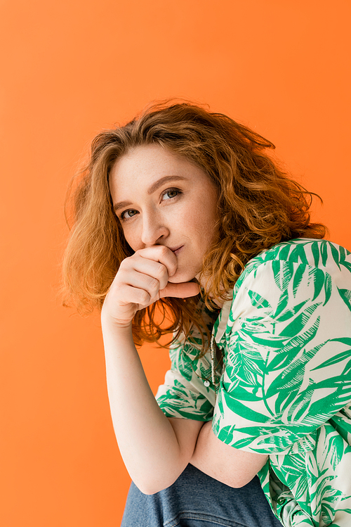Portrait of young redhead woman with no-makeup look wearing modern blouse with floral print and jeans while looking at camera isolated on orange, trendy casual summer outfit concept, Youth Culture
