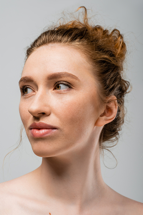 Portrait of young red haired and freckled woman with natural makeup and naked shoulders looking away and standing isolated on grey, natural beauty and individuality concept, Youth Culture
