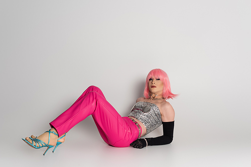 Fashionable drag queen in top and heels lying on grey background