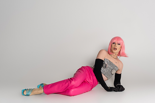 Trendy transgender person in sparkling top and gloves lying on grey background