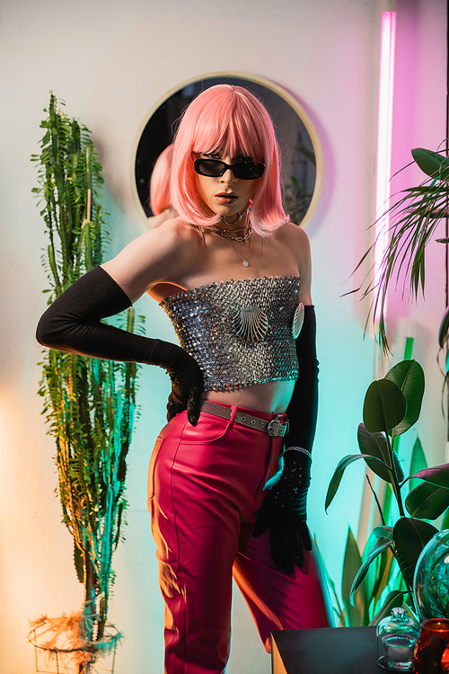 Fashionable drag queen in pink wig and shiny top posing at home