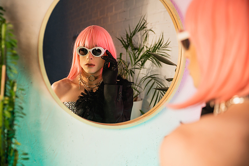 Blurred drag queen in pink wig wearing sunglasses near mirror at home