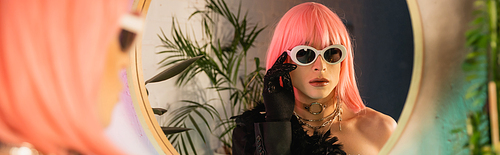 Fashionable drag queen in pink wig wearing sunglasses near mirror at home, banner