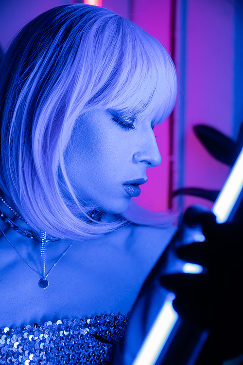 Portrait of drag queen in wig holding neon lamp at home