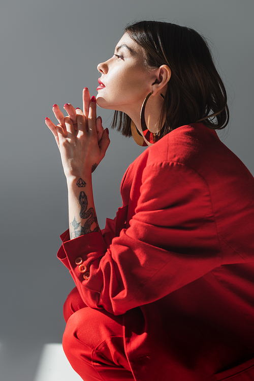 lady in red, young and tattooed woman with short hair posing in suit on grey background, generation z, trendy outfit, fashionable model, professional attire, executive style, side view