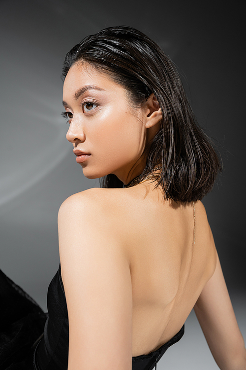 portrait of asian young woman with short brunette hair standing in black strapless dress on grey background, everyday makeup, wet hairstyle, charming model, natural beauty