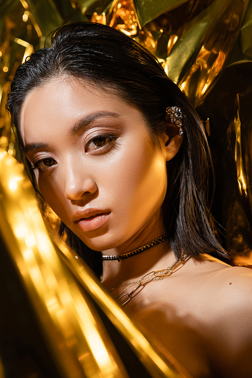 portrait of alluring asian young woman with wet short hair posing next to shiny yellow background, model, looking at camera, wrinkled golden foil, natural asian beauty
