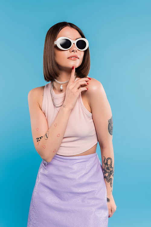 fashion trend, brunette young woman with short hair in tank top, skirt and sunglasses posing on blue background, casual attire, gen z fashion, personal style, everyday makeup, casual attire