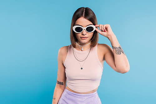 gen z fashion, brunette young woman with short hair in tank top, skirt and sunglasses posing on blue background, casual attire, stylish posing, personal style, portrait, fashionista