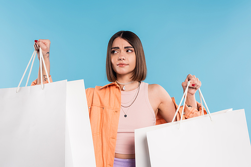 shopping spree, confused young woman in trendy outfit posing with shopping bags on blue background, casual attire, stylish, generation z, modern fashion, summer clothes